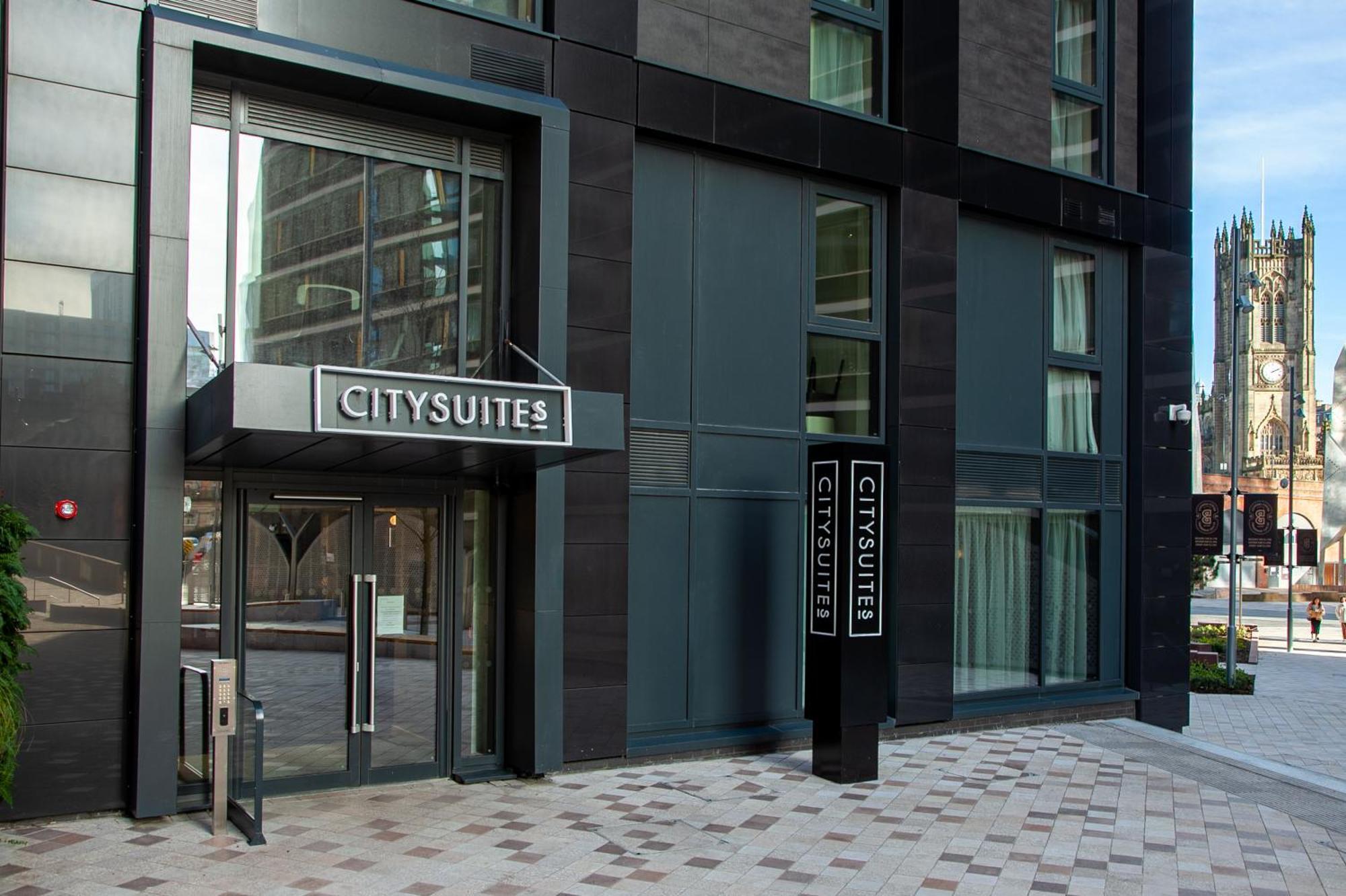 Citysuites 2 Aparthotel Salford (Greater Manchester) Exterior foto The photo shows the entrance to a modern building labeled "CITYSUITES." The entrance features large glass doors and a sleek, contemporary design. The building has dark exterior panels and large windows, suggesting a stylish and urban environment. The