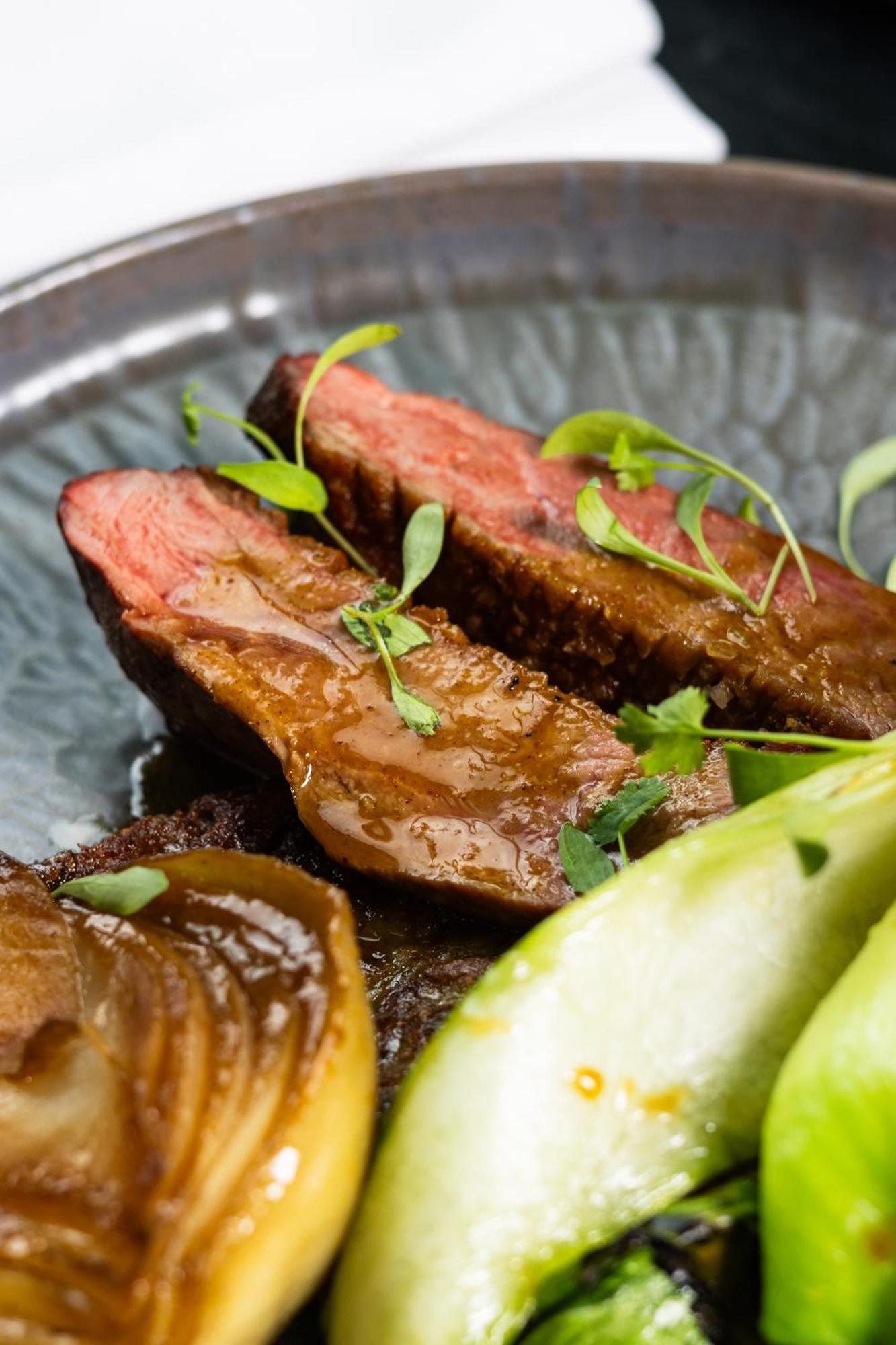 Citysuites 2 Aparthotel Salford (Greater Manchester) Exterior foto The photo features slices of meat, likely beef, presented on a decorative plate. The meat appears to have a rich brown sauce drizzled over it and is garnished with fresh herbs, adding a pop of green. There are also some slices of a light-colored vege