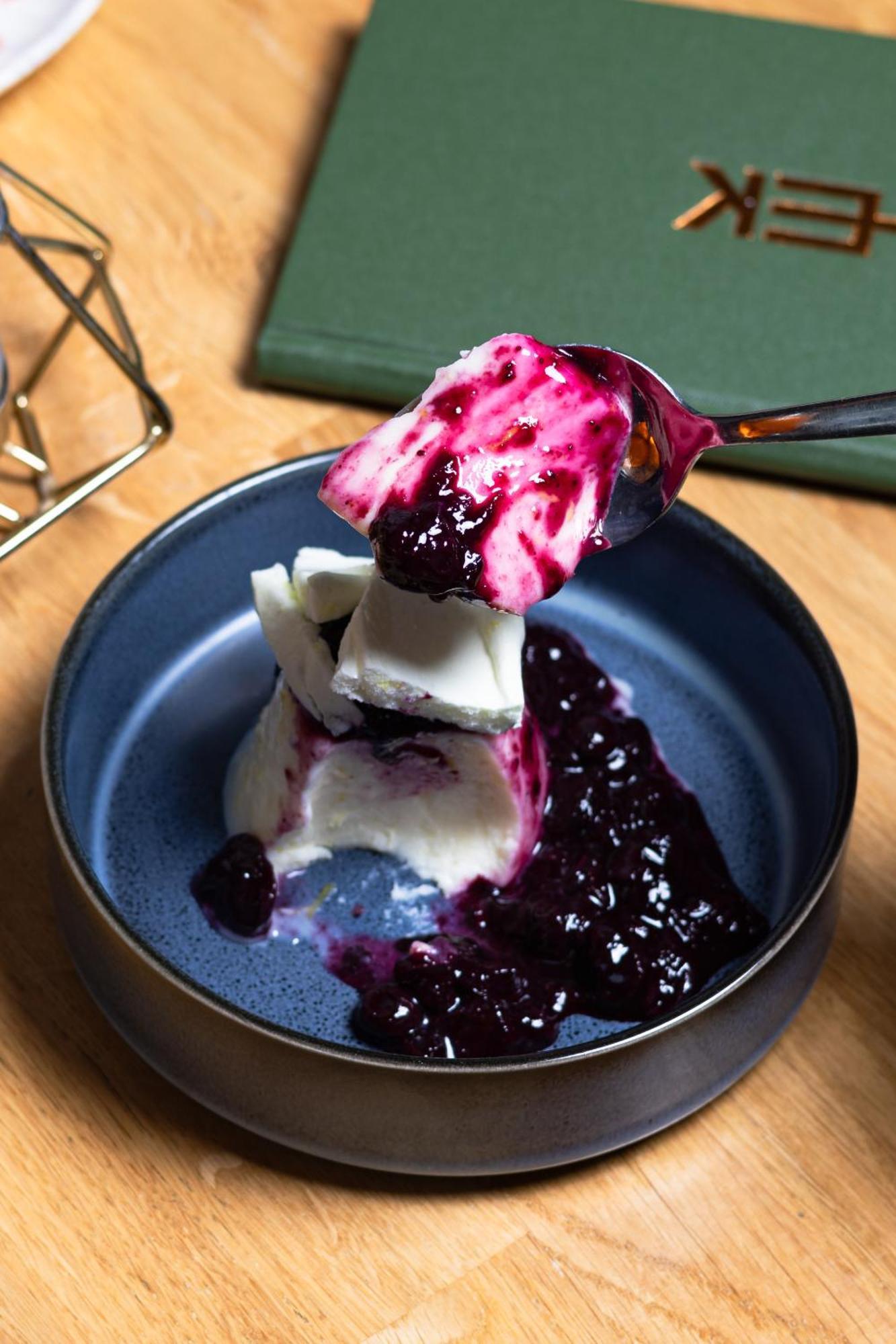 Citysuites 2 Aparthotel Salford (Greater Manchester) Exterior foto The photo shows a serving of dessert, likely a type of panna cotta or a creamy custard, partially dished out and accompanied by a rich berry sauce, possibly made from blueberries or blackberries. A spoon with some of the dessert and sauce is hovering